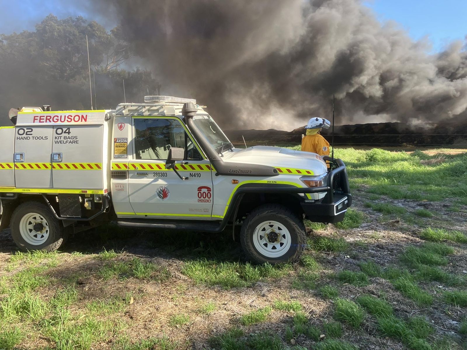 A Ferguson Bushfire Brigade light tanker parked on grass with heavy smoke rising behind it